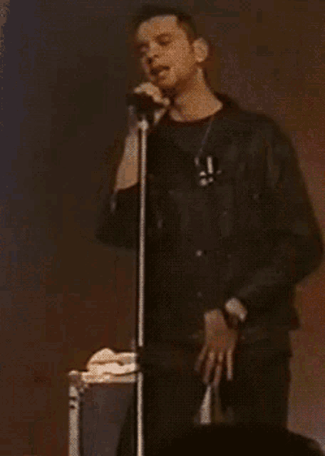 a man in a leather jacket singing into a microphone with the letter a on his shirt