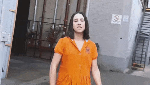 a woman in an orange jumpsuit is standing in a parking lot .