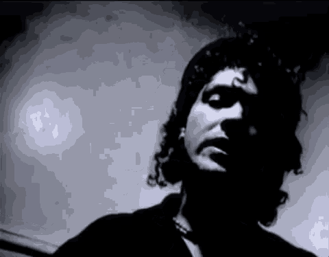 a black and white photo of a man with curly hair and a necklace .