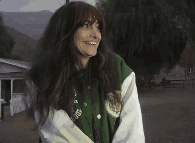 a woman wearing a green and white varsity jacket smiles for the camera