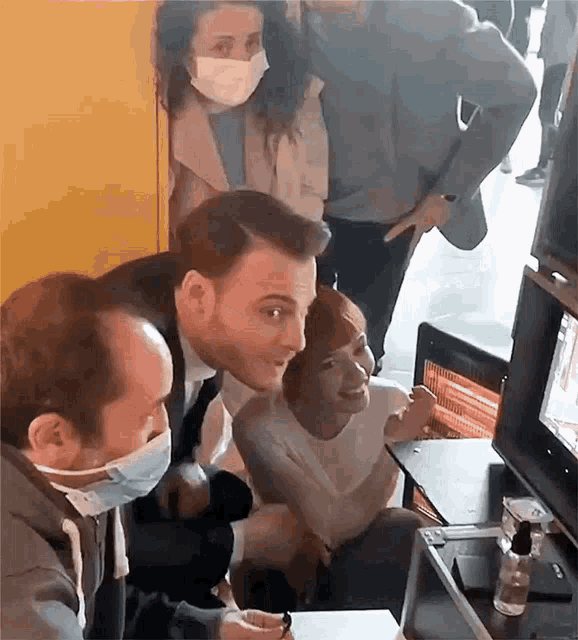 a group of people wearing face masks are sitting around a table with a laptop .