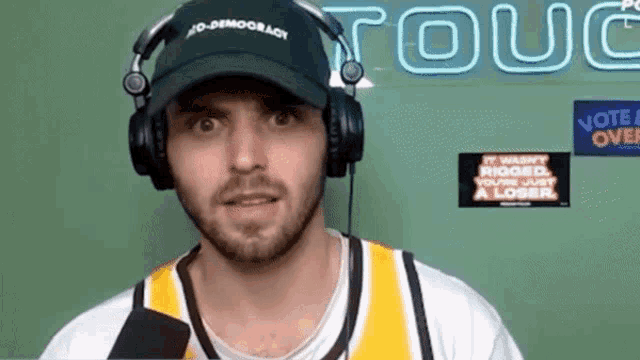 a man wearing headphones and a no democracy hat talks into a microphone