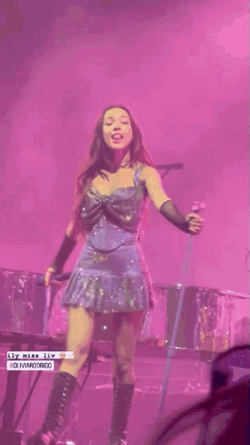 a woman in a purple dress and black gloves stands on stage