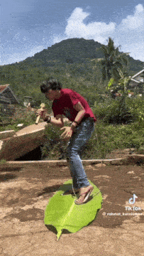 a man in a red shirt is standing on a green banana leaf