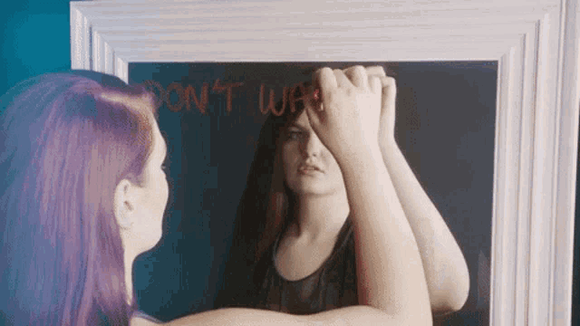 a woman is looking at her reflection in a mirror that says " do n't wait "
