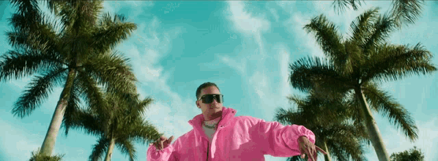 a man wearing a pink jacket and sunglasses stands in front of palm trees
