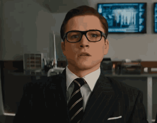 a man wearing glasses and a suit has a shocked look on his face