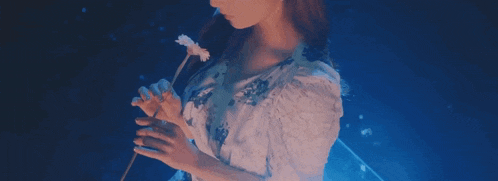 a woman in a white dress is holding a white flower .