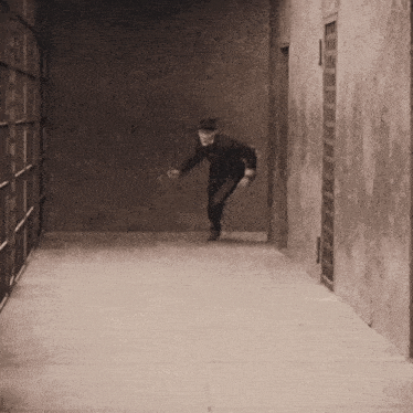 a black and white photo of a man in a top hat running down a hallway