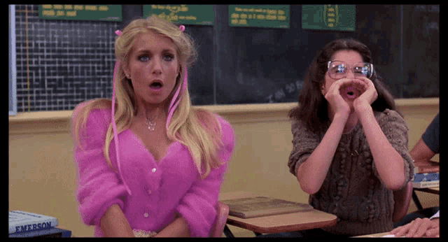 a woman in a pink sweater is sitting in front of a blackboard with the name emerson on it