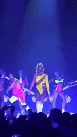 a woman in a yellow jumpsuit is dancing on stage
