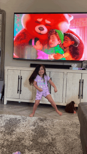 a little girl is dancing in front of a tv screen showing a red panda