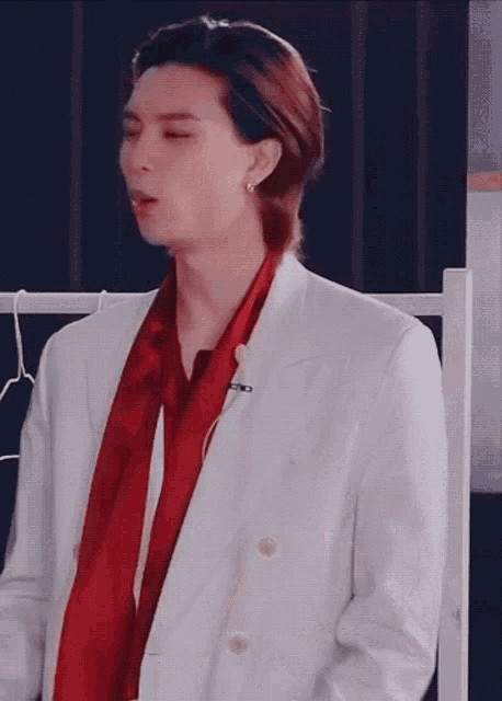 a man in a white suit and red scarf is standing in front of a black wall .