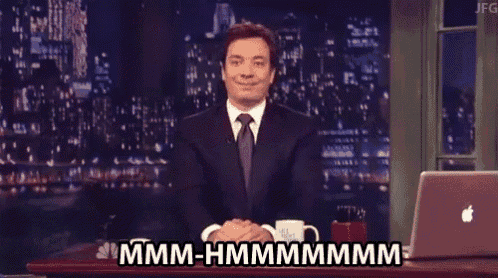 a man in a suit and tie is sitting at a desk with a laptop and says hmm-hmmmmmm