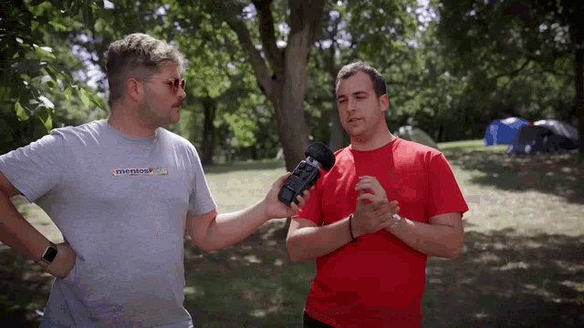 a man wearing a grey t-shirt with the word emerson on it talks to another man wearing a red shirt