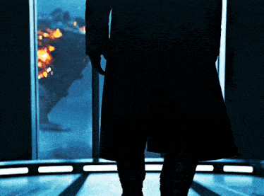 a man in a black coat stands in front of a large window