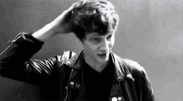 a black and white photo of a man in a leather jacket scratching his head .