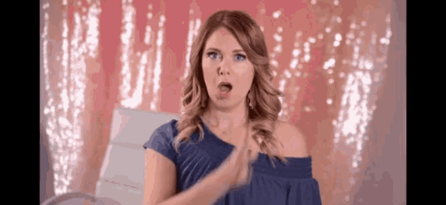 a woman wearing a blue off the shoulder top is clapping her hands