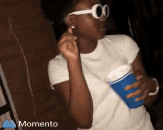 a girl wearing sunglasses is holding a blue cup in her hand