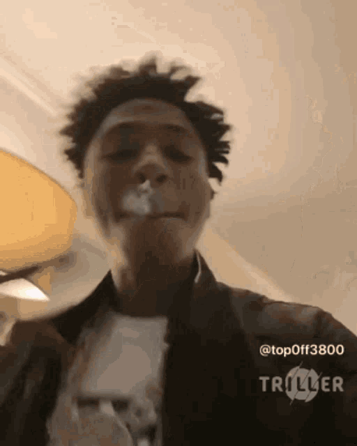 a young man is smoking a cigarette in a room with a lamp in the background .