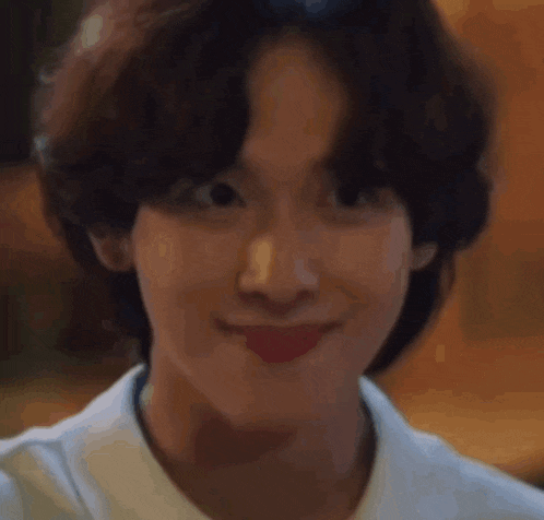 a young man in a white shirt is smiling and looking down .