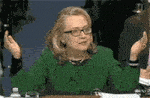 a woman in a green jacket and glasses is sitting at a table with her arms outstretched .