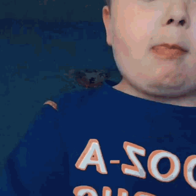 a young boy wearing a blue shirt with the words `` a-soon '' on it .