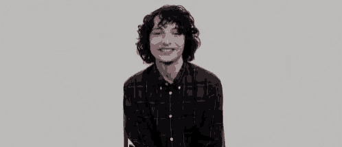 a young man with curly hair is wearing a plaid shirt and smiling while sitting down .