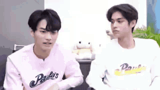 two young men are sitting next to each other in a room . one of the men is wearing a pink sweater .