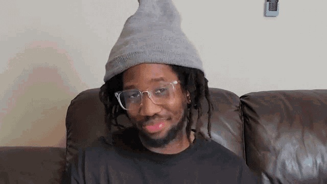 a man wearing glasses and a hat is sitting on a couch .