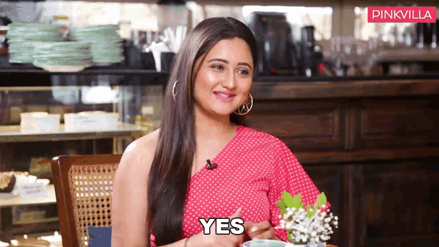 a woman in a pink polka dot dress is sitting at a table and says yes
