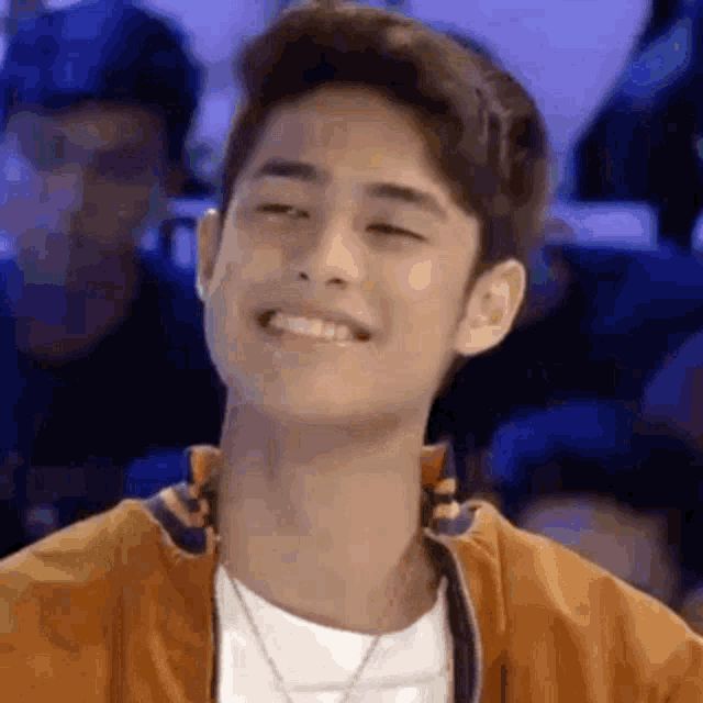 a young man is smiling and looking at the camera while wearing an orange jacket .
