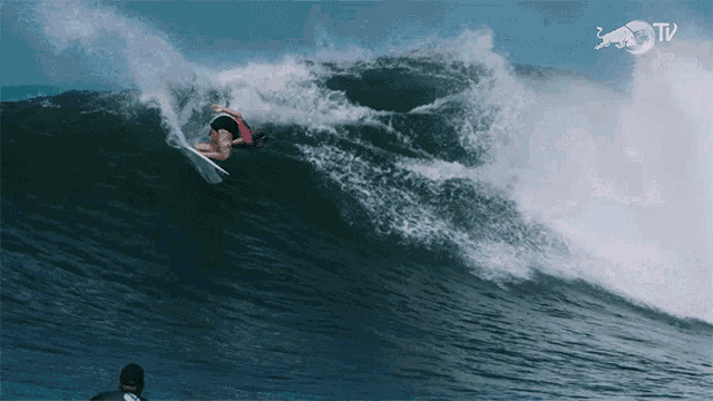 a surfer rides a wave with a red bull tv logo behind her