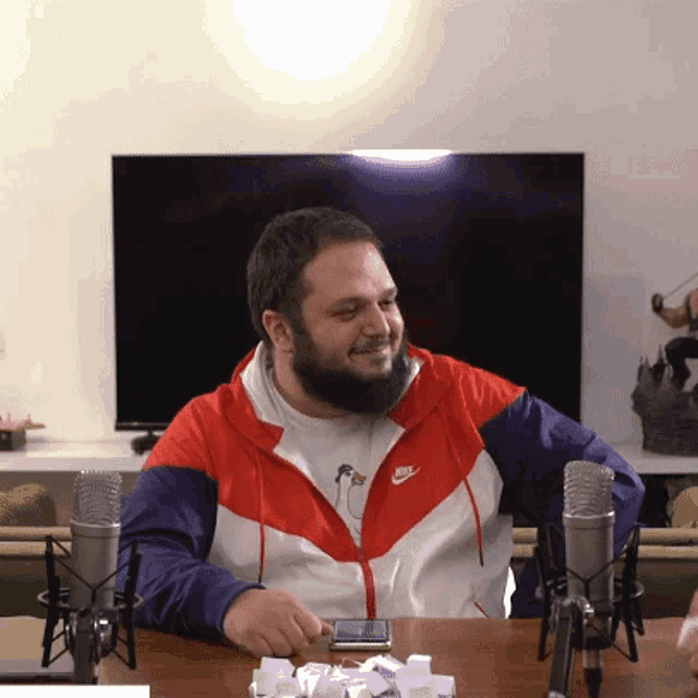 a man wearing a nike jacket sits at a table in front of two microphones