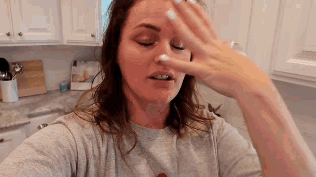 a woman in a grey shirt is covering her face with her hand