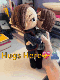a person holding two crocheted dolls with the words hugs here written on the bottom