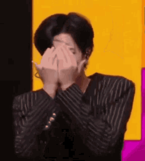 a man is covering his face with his hands in front of a yellow and pink background .