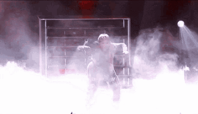 a man is dancing on a stage in a cage with smoke coming out of it