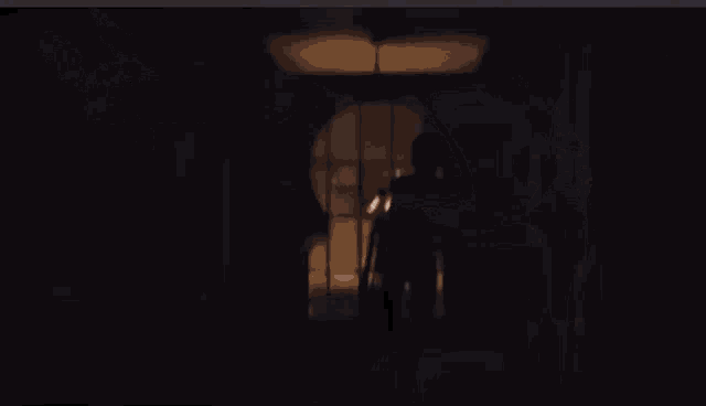 a person is standing in a dark room with a light coming out of the window .