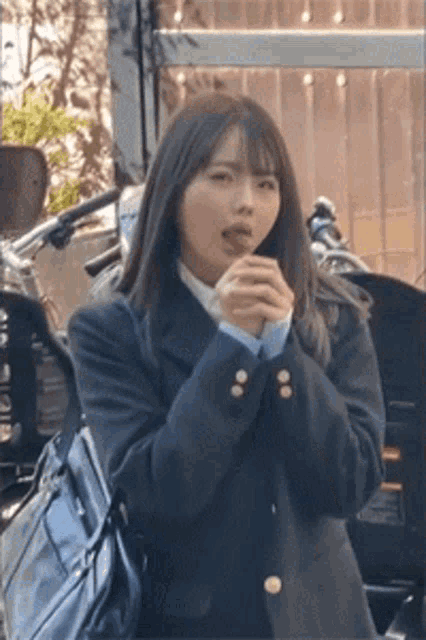 a girl in a school uniform is standing next to a motorcycle and holding her hands together .