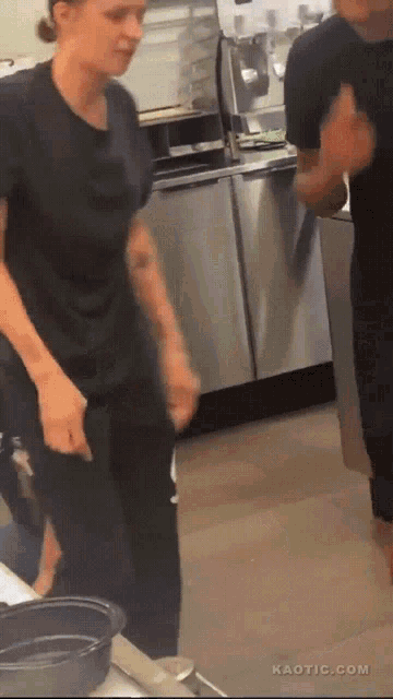 a man and a woman are dancing in a kitchen with kaotic.com written on the bottom right
