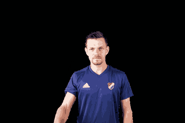 a man wearing a blue adidas shirt salutes with his hand