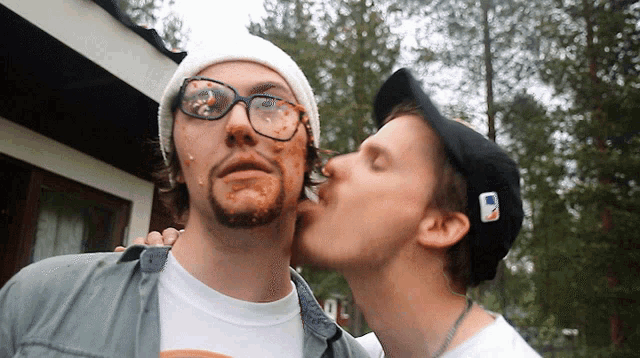 a man wearing a black hat with the letter m on it kisses another man
