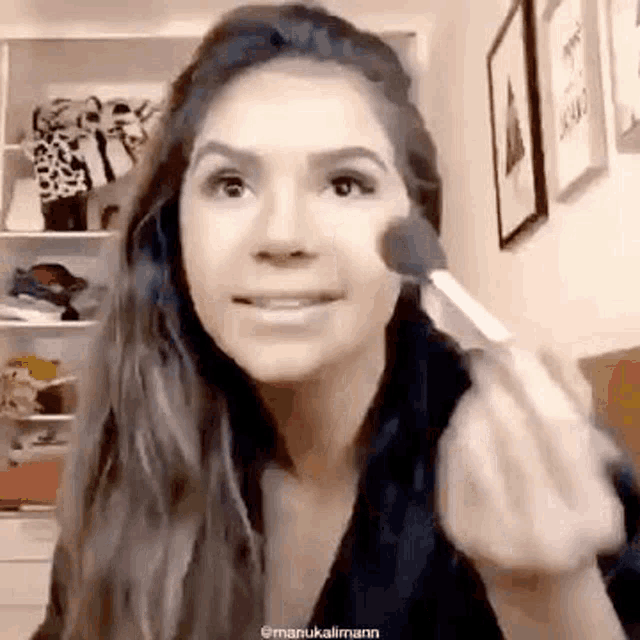 a woman is applying makeup to her face with a brush while looking at the camera .