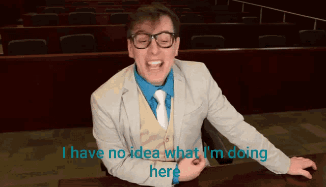 a man in a suit and tie is sitting at a desk with the words i have no idea what i 'm doing here