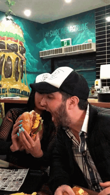 a man and a woman are eating a hamburger in front of a wall that says #share the burger love