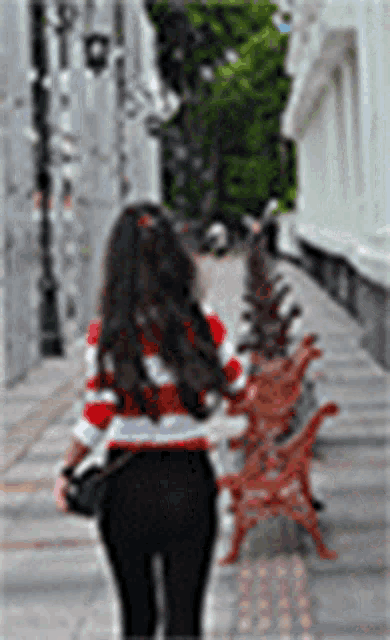 a woman wearing a red and white striped shirt is walking down a sidewalk