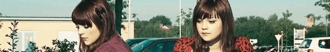 two women are standing next to each other in a parking lot with trees in the background