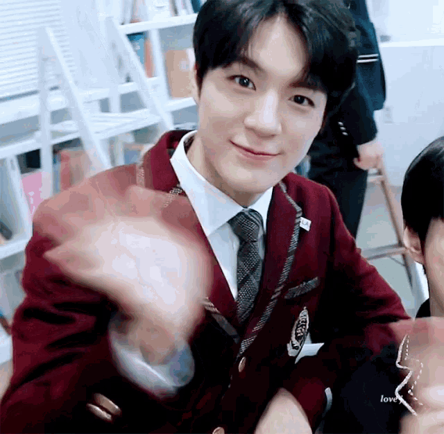 a young man wearing a suit and tie is waving his hand