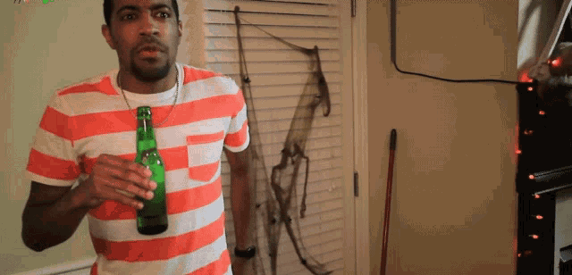 a man in an orange and white striped shirt holds a green beer bottle